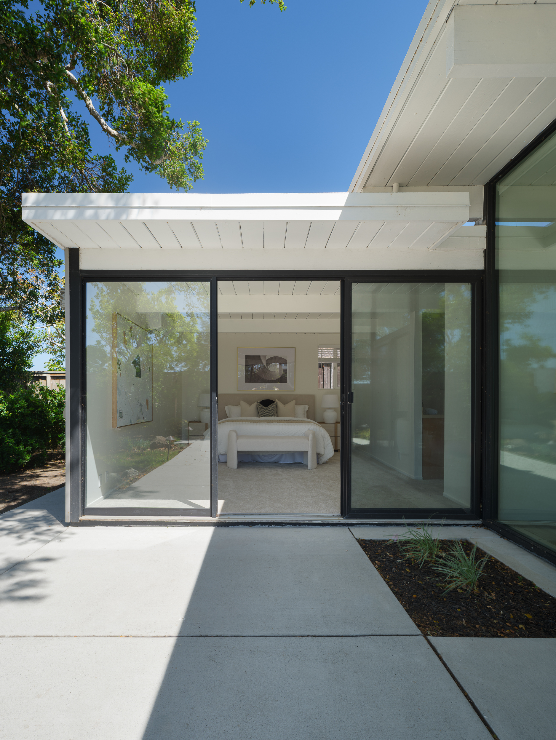 Patio view through black-framed doors toward calm neutral bedroom staging and soft light