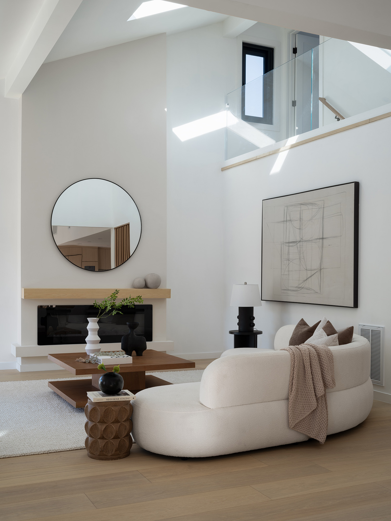 Double-height living room with curved cream sofa, wood table, skylight, and open floor area preserving bright sightlines