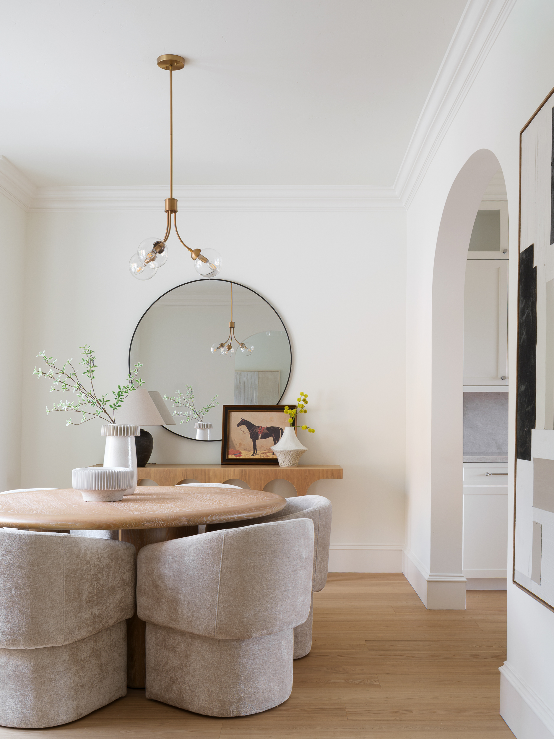 Round light-oak dining table with greige chairs, soft neutrals, and sculptural staging restraint