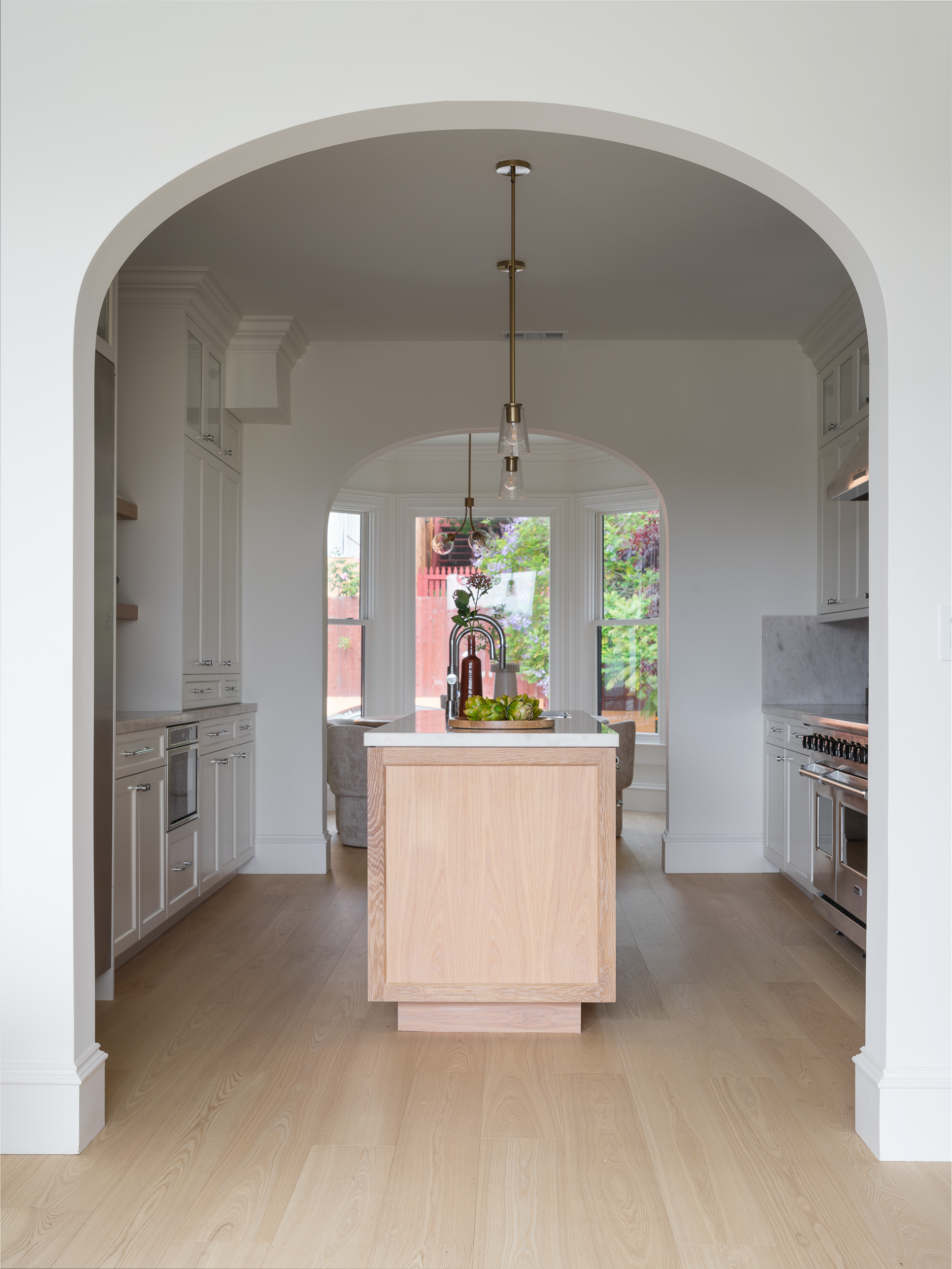 Cream kitchen with pale oak floors and arched openings staged for clear Bay Area flow