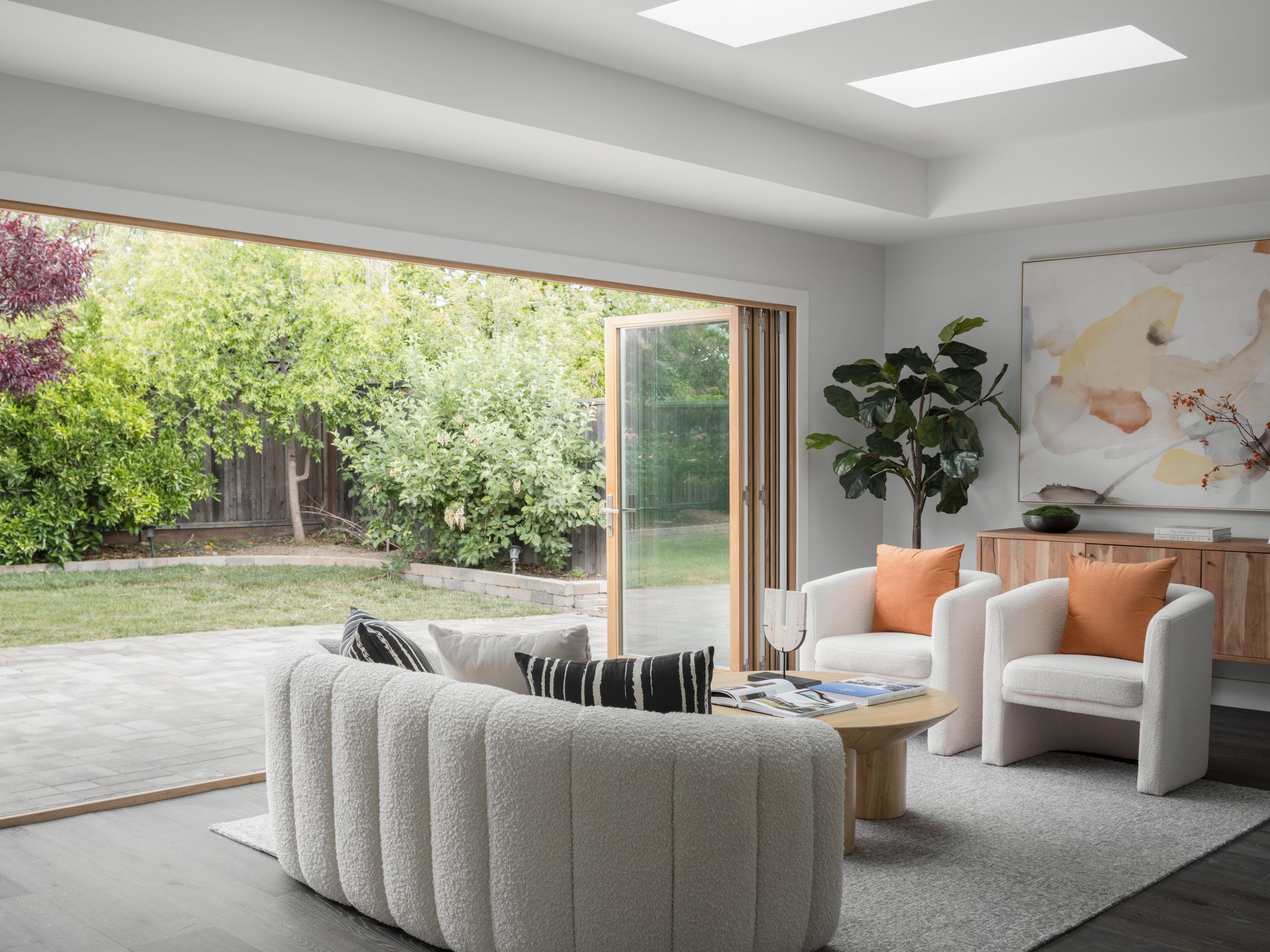 Bright living room with cream boucle seating, skylights, and folding doors open to the backyard for summer staging flow