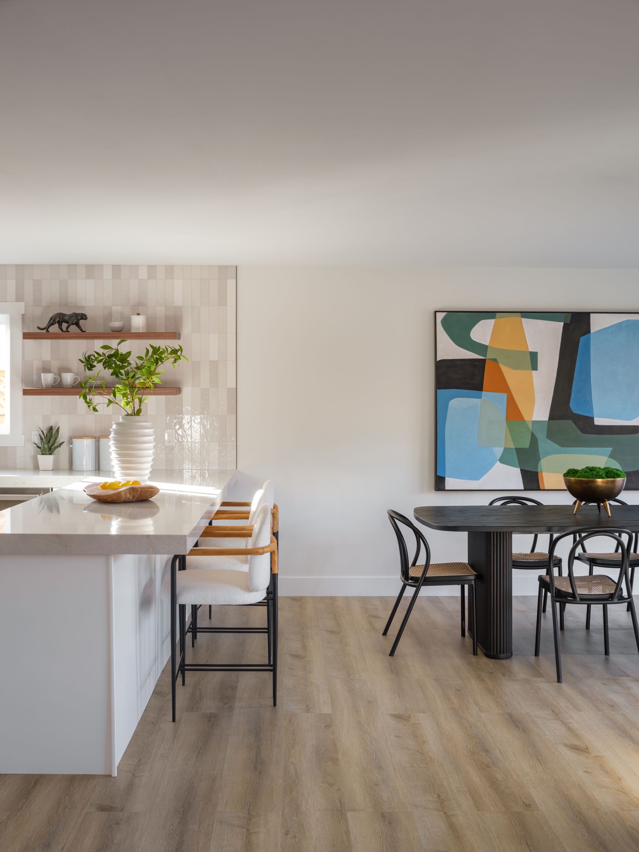 White kitchen island and round black dining table with cane chairs define work and eating areas in an open-plan room.