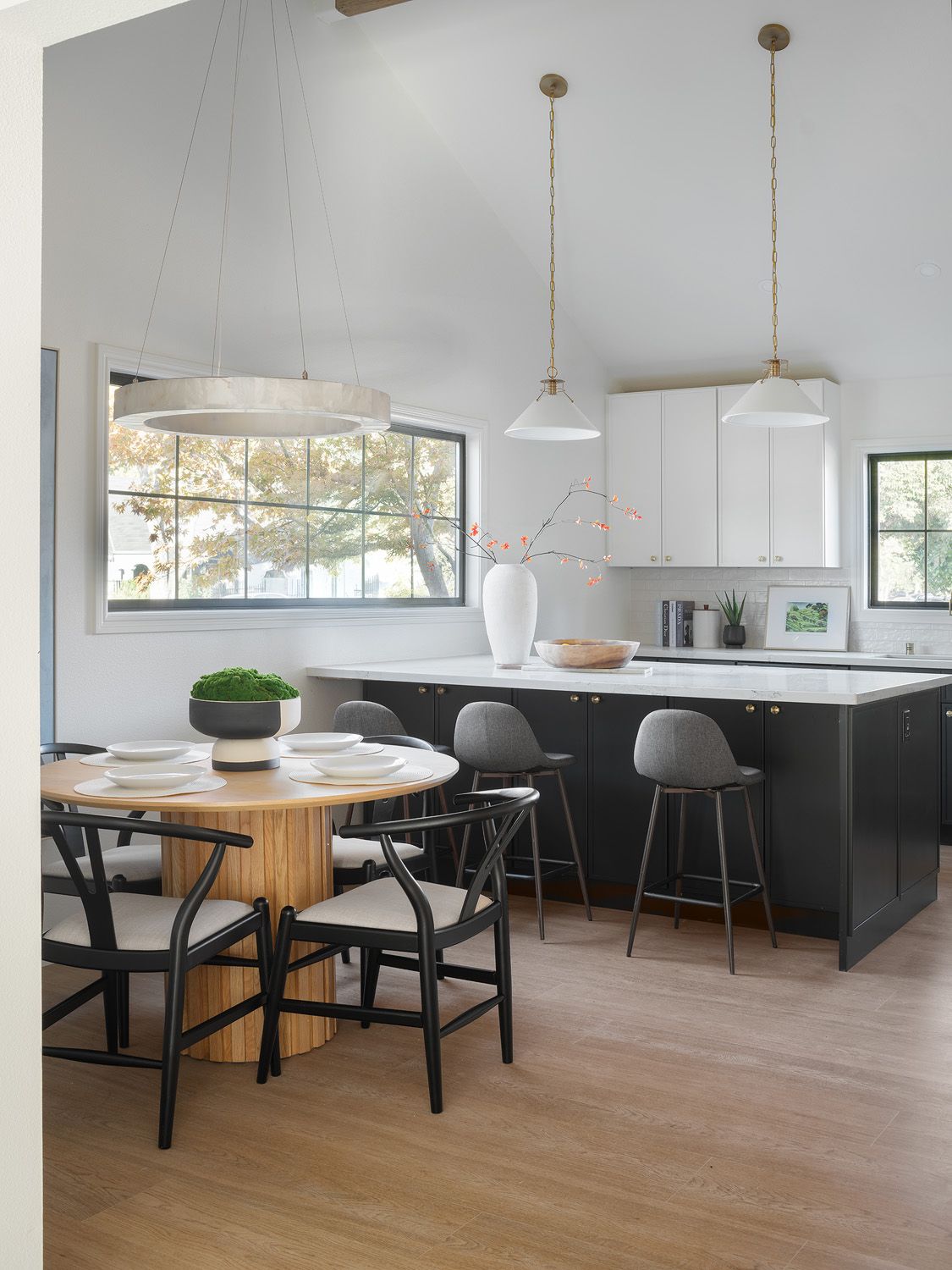 Round wood dining table beside a charcoal kitchen island with gray barstools, showing separate dining and counter seating.