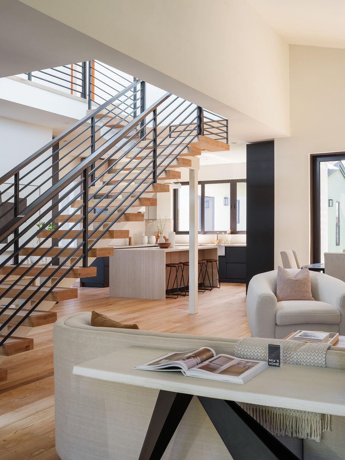 Large open living area with curved sofa, floating oak stairs, black railings, and modern kitchen