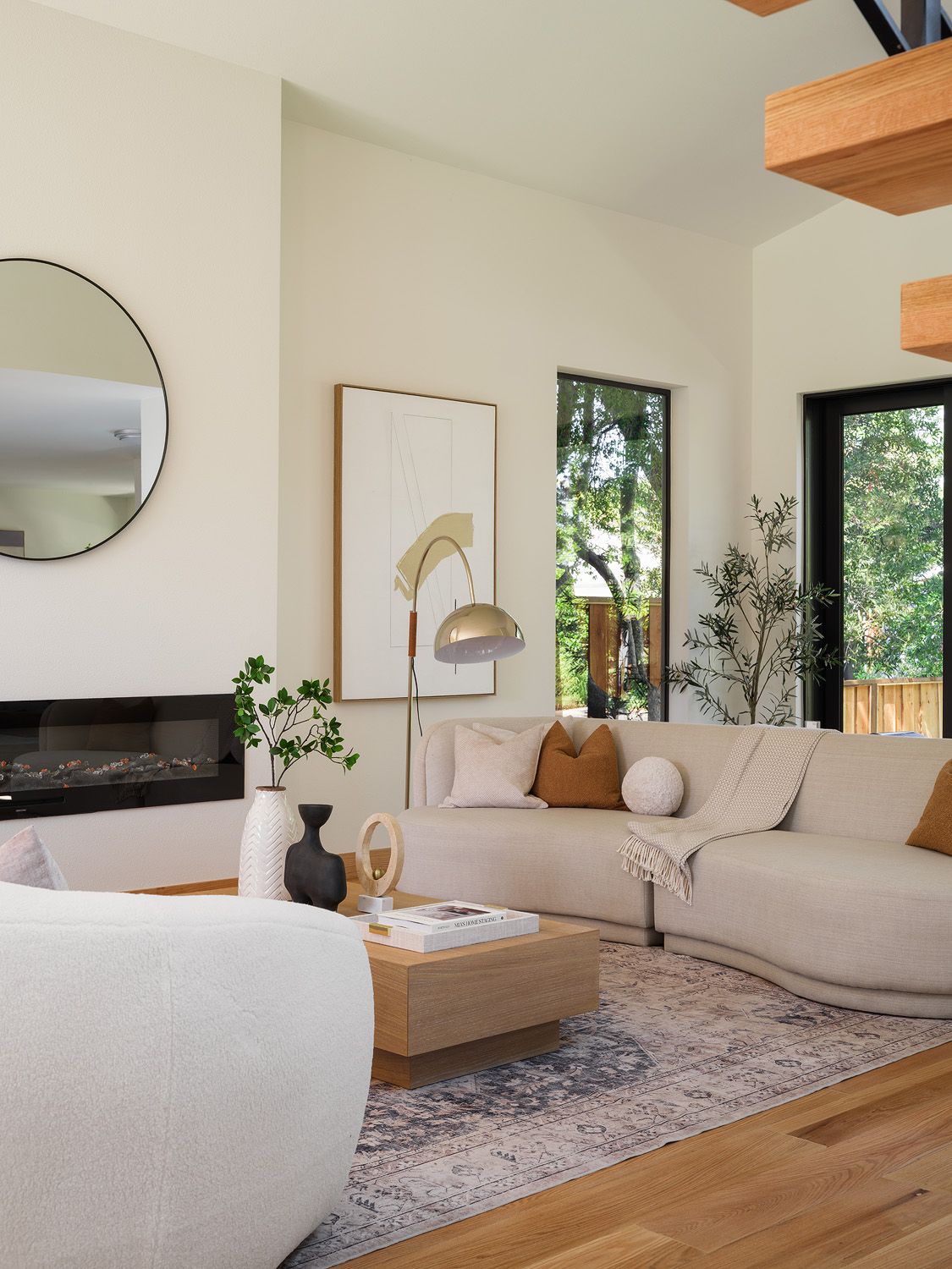 Cream sectional, pale oak table, rust pillows, and black fireplace form a balanced earth-tone living room palette