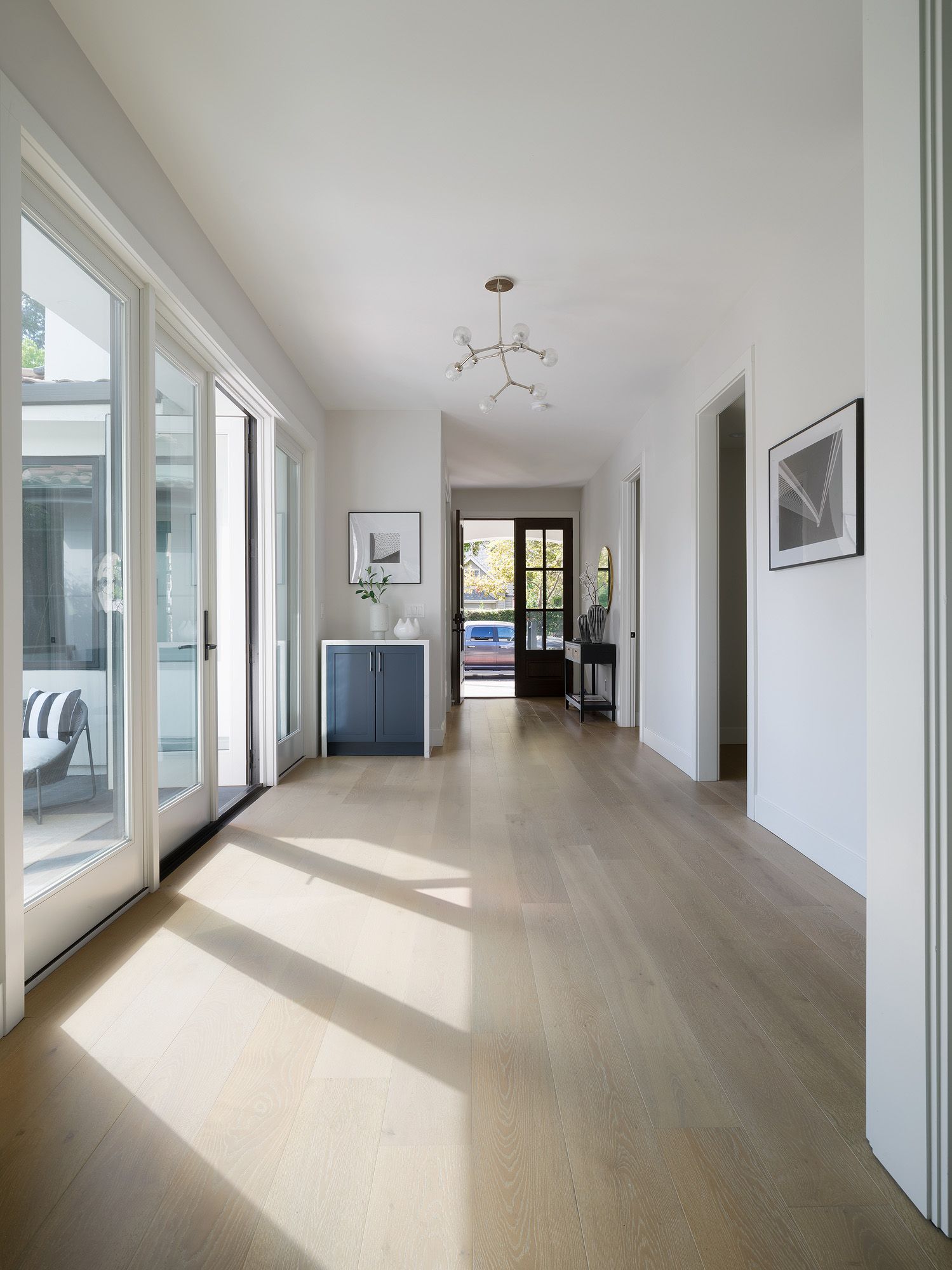 Long entry hall with pale oak floors, edited furnishings, abstract art, and clear traffic paths