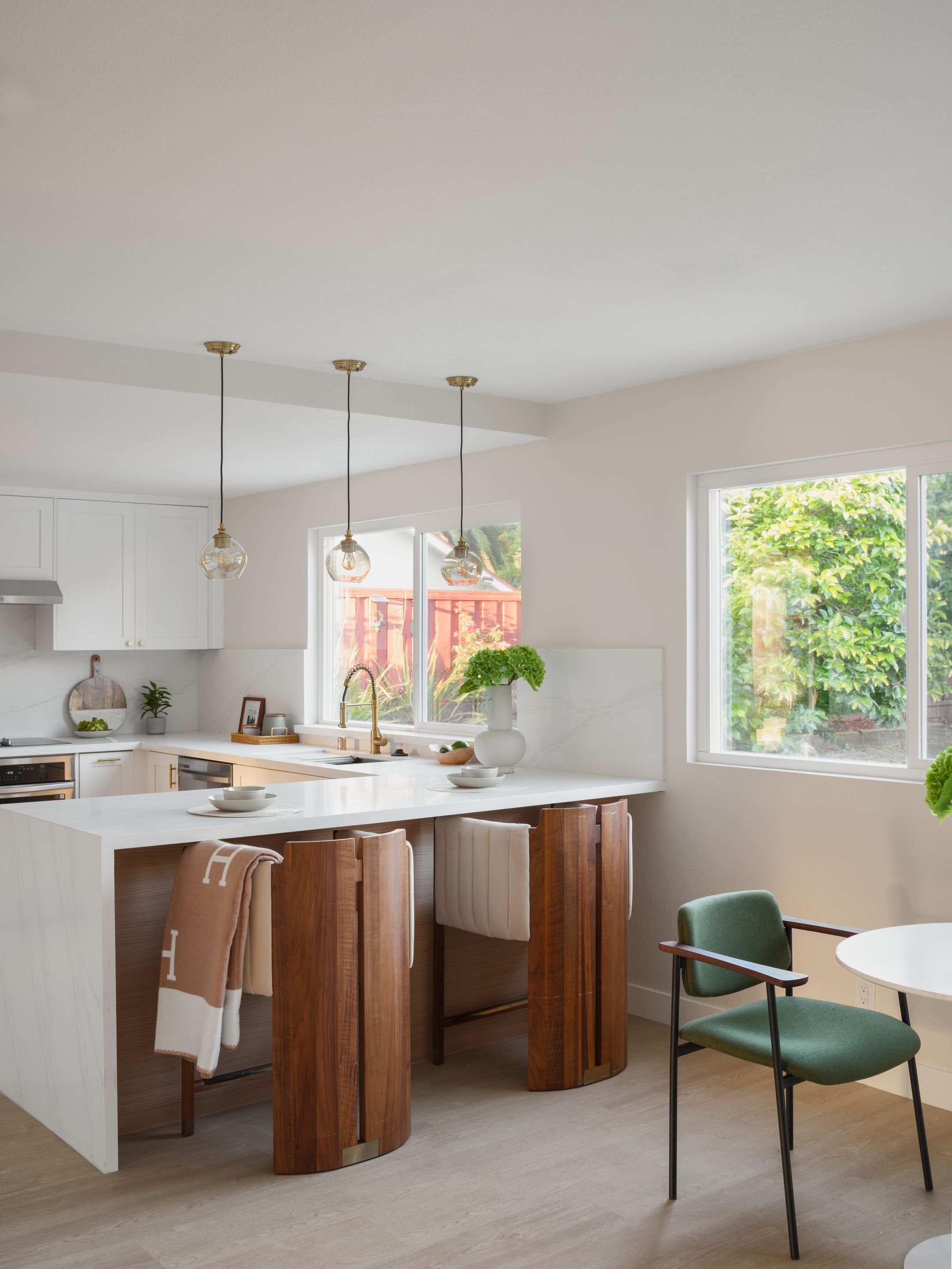 White waterfall kitchen island with walnut stools and garden windows keeps summer staging fresh and uncluttered