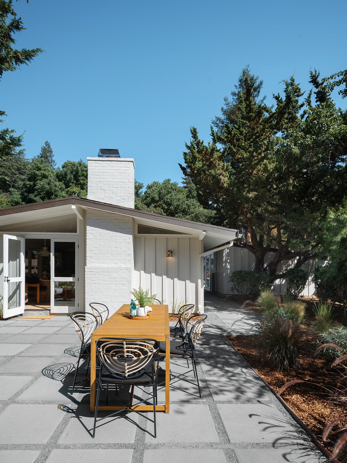 Wood patio dining table outside open glass doors, creating a clear indoor-outdoor route to the garden