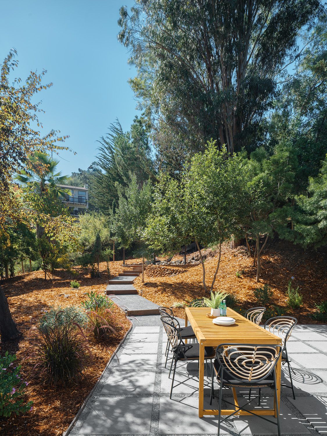 Sunny garden patio with slatted wood dining table and landscaped path supporting buyer-ready seasonal staging