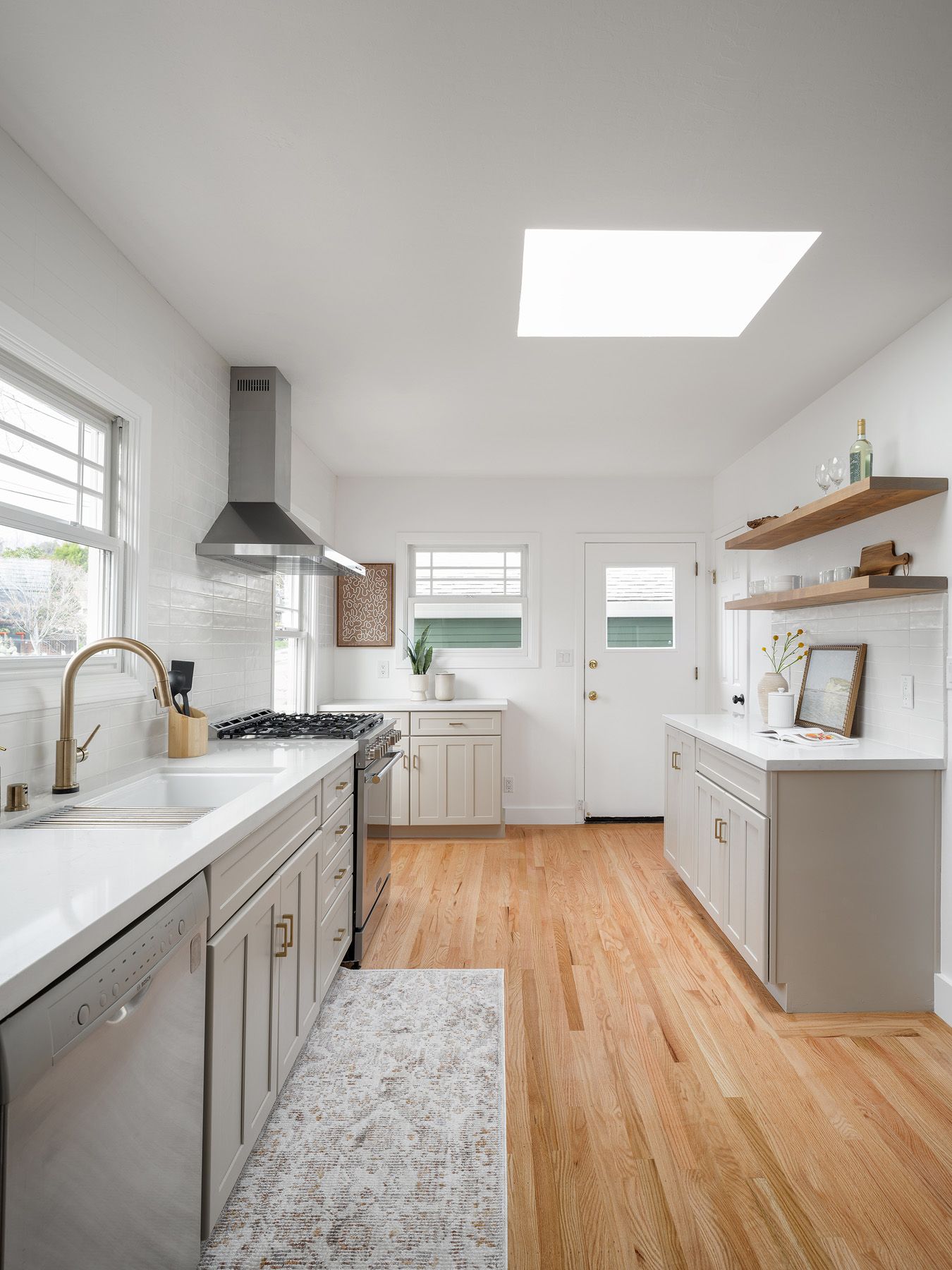 Bright galley kitchen with white tile, floating wood shelves, and clear counters for edited holiday staging