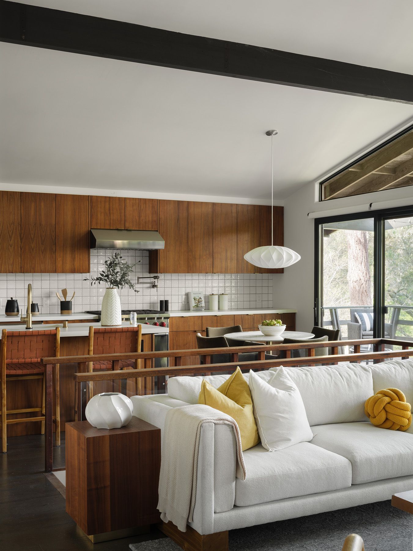 Cream sofa and woven barstools share an open view with walnut kitchen cabinets, connecting soft textures across adjoining spaces