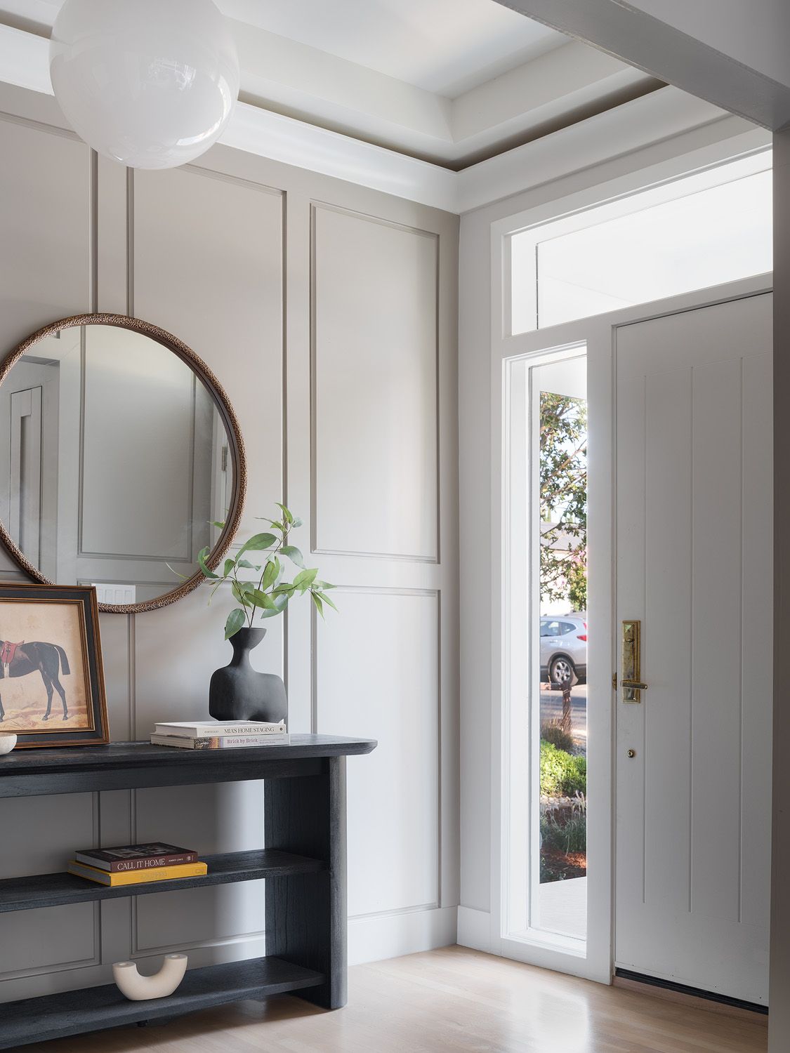 Slim black console and round woven mirror in a bright foyer arranged for an open, functional arrival