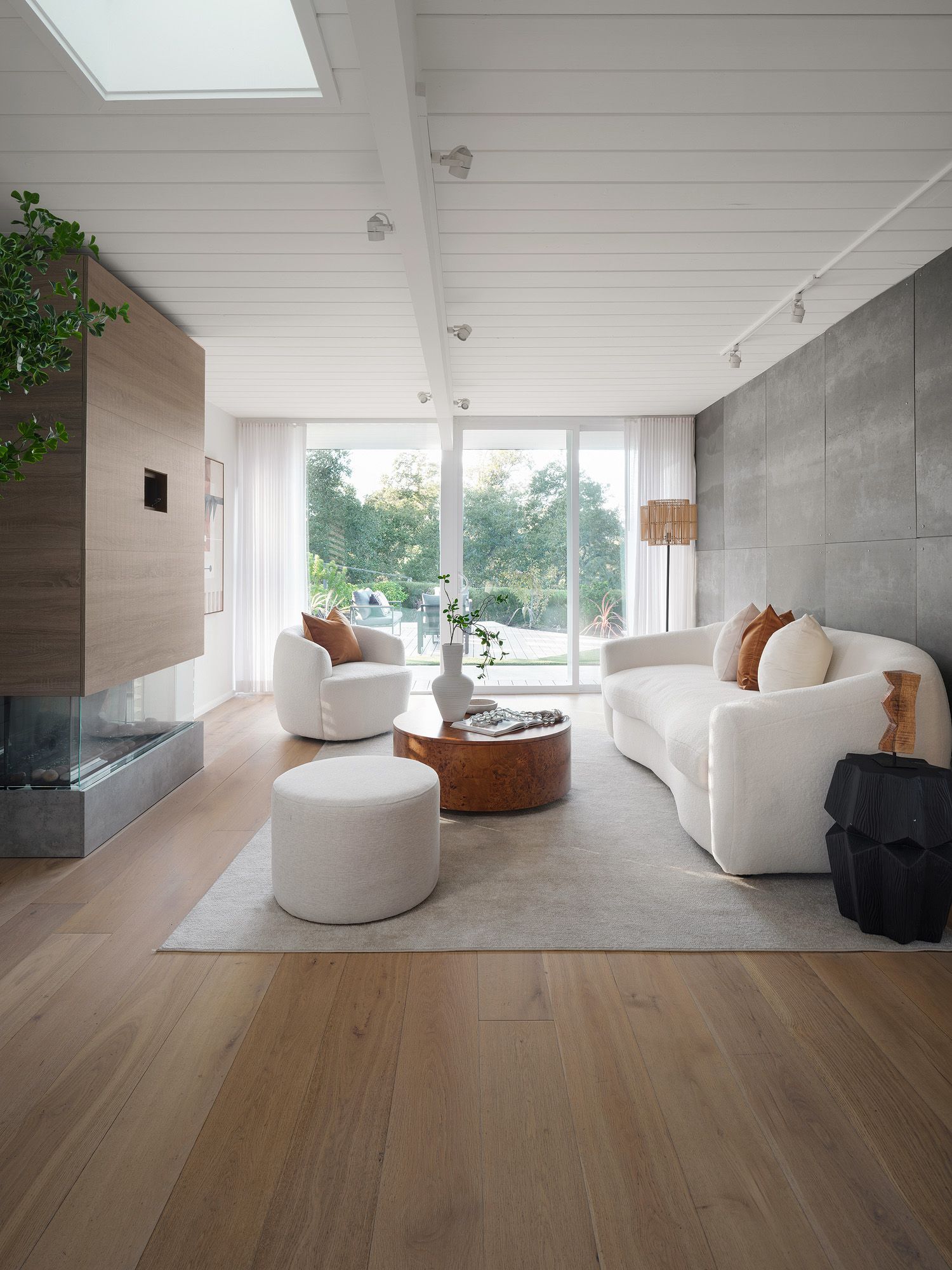Curved white sofa and rounded burl table soften a modern living room framed by concrete and straight glass doors