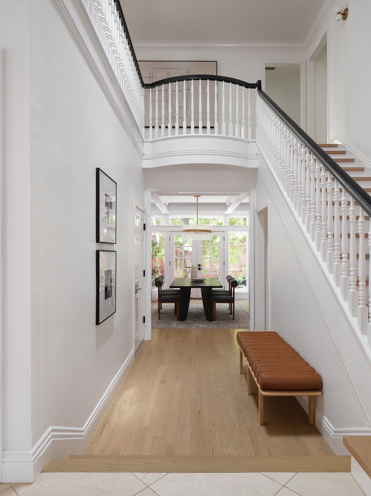 Bright foyer with white staircase, cognac bench, and an unobstructed sightline into the dining room